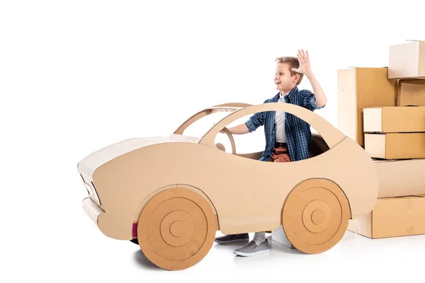 Boy sitting in cardboard car and waving on white — Stock Photo