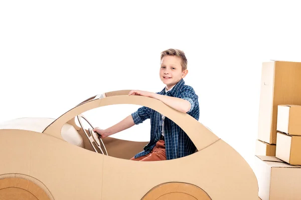 Sorrindo menino sentado no carro de papelão e olhando para a câmera isolado no branco — Fotografia de Stock