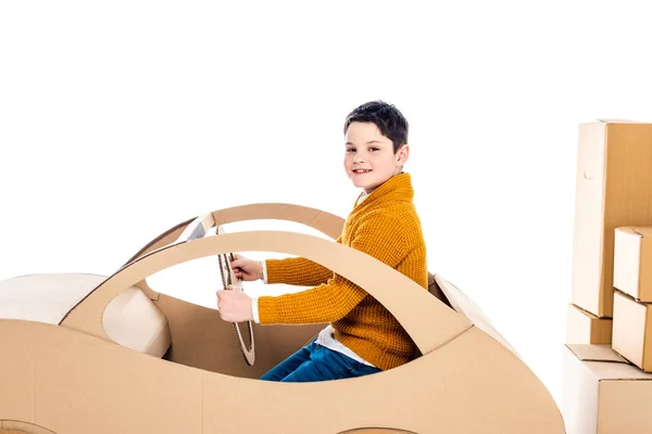 Мальчик смотрит на камеру, сидит и играет с картонным автомобилем возле пакетов Isolated On White — стоковое фото