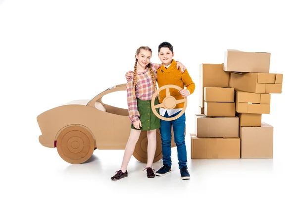 Enfants heureux posant avec volant près de voiture en carton sur blanc — Photo de stock