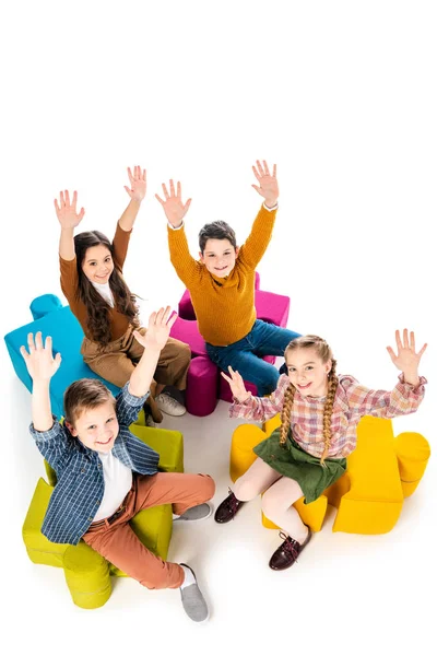 Opinião de ângulo elevado de miúdos felizes com as mãos outstretched que sentam-se em pufes do enigma de serra de vaivém no branco — Fotografia de Stock
