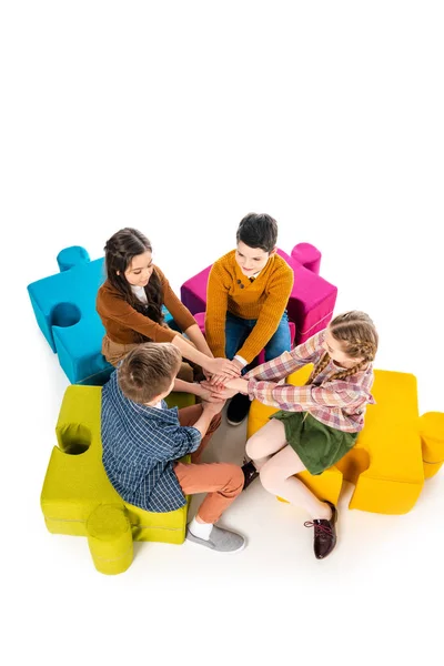Vue à angle élevé des enfants assis sur des poufs puzzle et empilant les mains isolées sur blanc — Photo de stock
