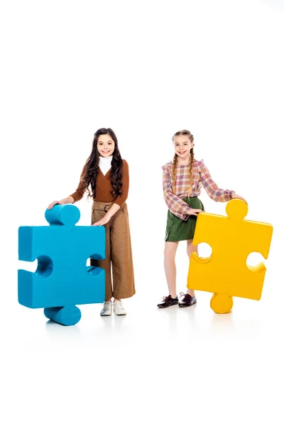 Smiling kids with jigsaw puzzle pieces looking at camera on white — Stock Photo