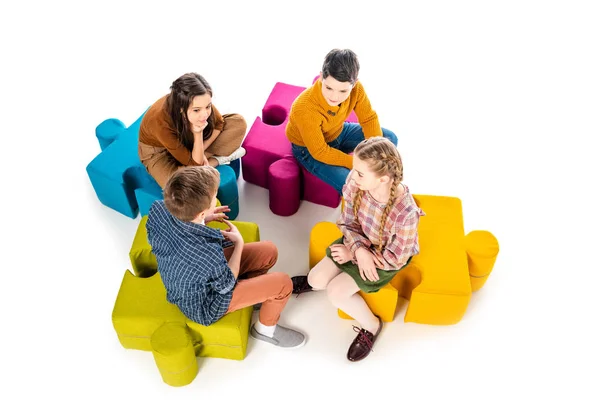 Vista de ángulo alto de los niños sentados en pufs rompecabezas y hablando aislado en blanco - foto de stock