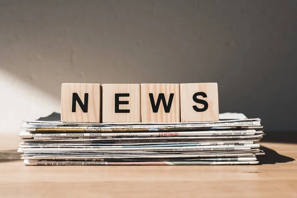 Wooden blocks with news lettering on pile of print newspapers — Stock Photo