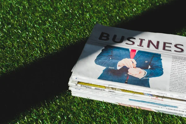 Pile de journaux d'affaires imprimés sur herbe verte fraîche avec ombre — Photo de stock
