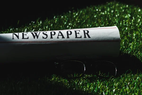 Gros plan du journal roulé sur l'herbe verte près des lunettes — Photo de stock