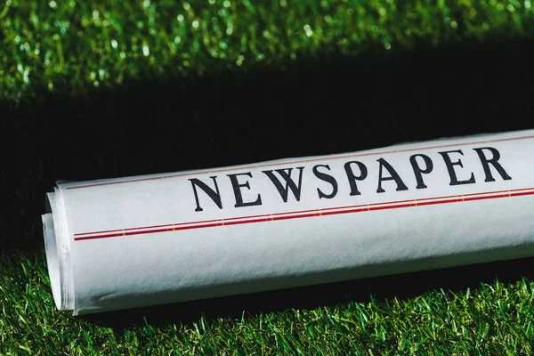 Close up of rolled newspaper on green grass with shadow — Stock Photo