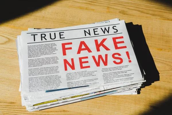 Pila de periódicos con noticias falsas y verdaderas en la mesa de madera - foto de stock