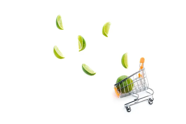 Top view of lime slices near decorative small shopping cart isolated on white — Stock Photo