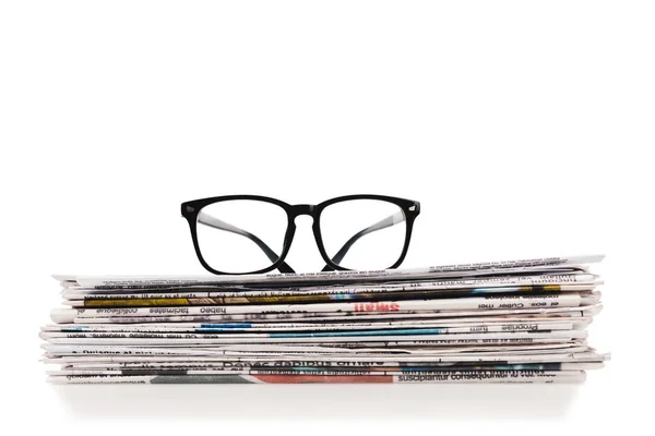 Stack of daily newspapers with glasses on top isolated on white — Stock Photo