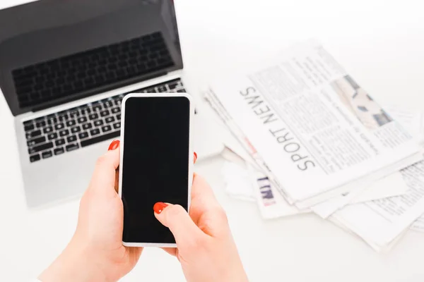 Foyer sélectif de la femme tenant smartphone avec écran blanc près de l'ordinateur portable et les journaux — Photo de stock