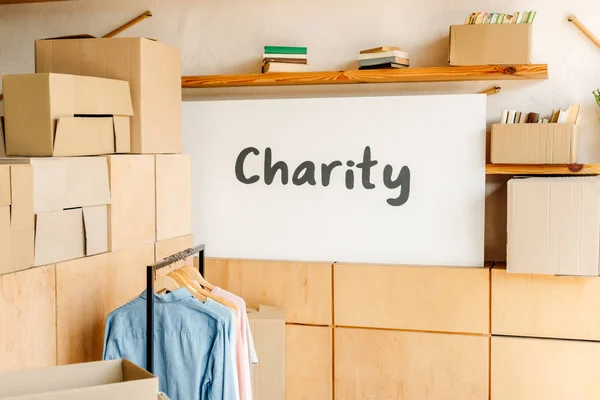 Wooden cabinets, carton boxes, rack with shirts and placard with charity inscription — Stock Photo