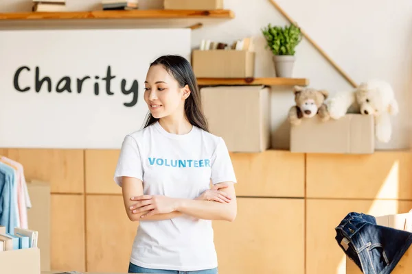 Belle femme asiatique en t-shirt blanc avec inscription volontaire debout avec bras croisés — Photo de stock
