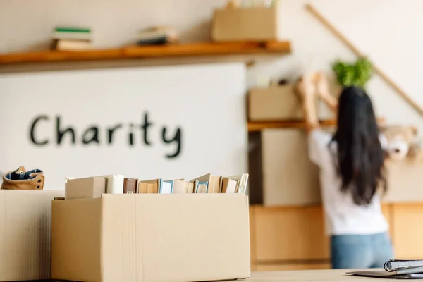 Selective focus of cardboard box with books and volunteer working in charity center — Stock Photo