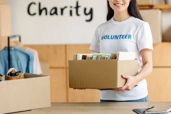 Vue recadrée de jeunes bénévoles tenant une boîte en carton avec des livres — Photo de stock