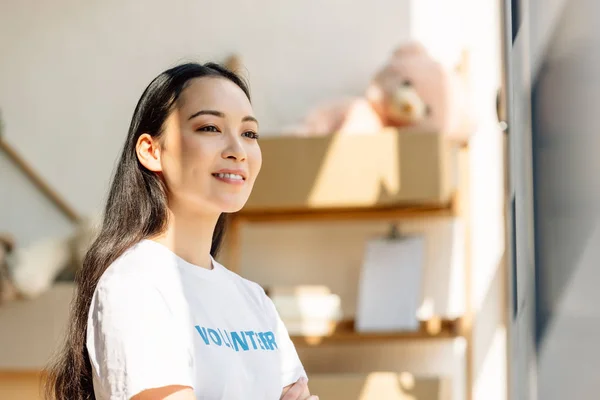 Bela asiático voluntário sorrindo enquanto de pé em sol e olhando para longe — Fotografia de Stock