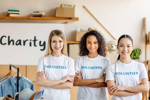 Tres hermosas chicas voluntarias multiculturales con los brazos cruzados sonriendo y mirando a la cámara - foto de stock