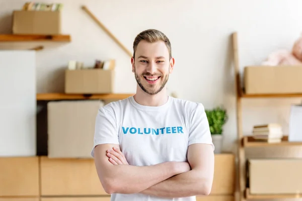 Schöner junger Freiwilliger mit verschränkten Armen, lächelnd und in die Kamera blickend — Stockfoto
