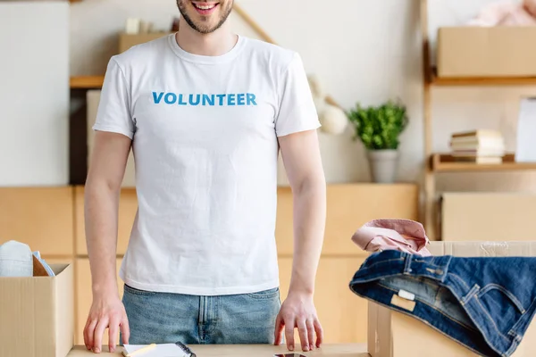 Обрезанный вид добровольца, стоящего рядом с картонными коробками с одеждой — стоковое фото