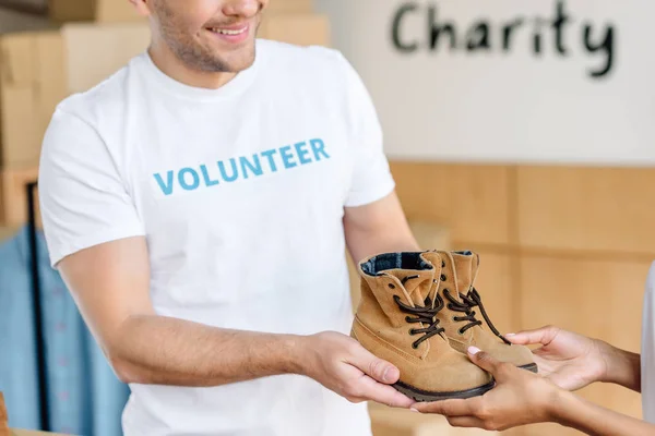 Vista cortada de dois voluntários multiculturais segurando sapatos infantis — Fotografia de Stock