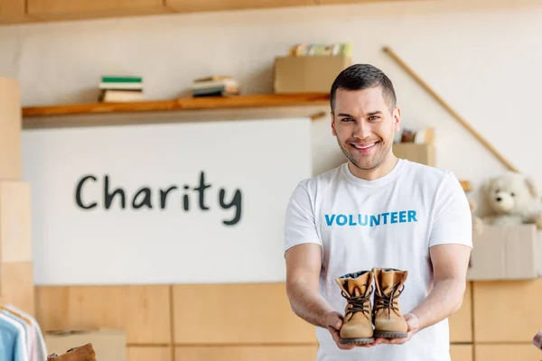 Симпатичный, веселый волонтер держит детскую обувь и смотрит в камеру — стоковое фото