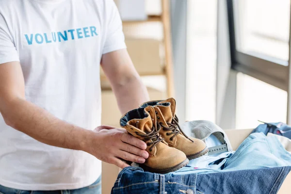 Обрезанный вид волонтера, держащего детскую обувь, стоя рядом с картонной коробкой с джинсами — стоковое фото