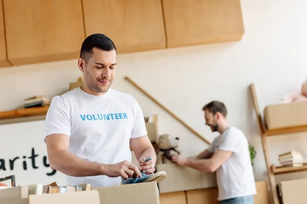 Selective focus of handsome volunteer unpacking cardboard box with footwear — Stock Photo