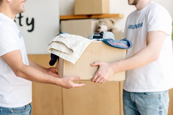 Cropped view of volunteers holding cardboard box with clothes in charity center — Stock Photo