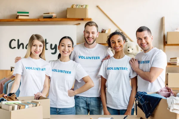 Cinco jóvenes voluntarios multiculturales de pie juntos, sonriendo y mirando a la cámara - foto de stock