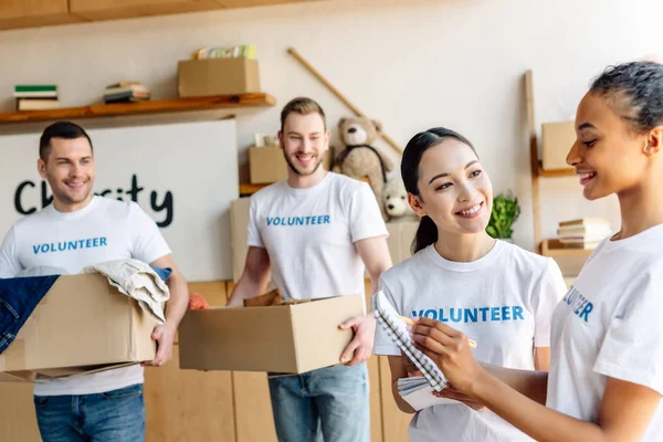 Enfoque selectivo de voluntarios alegres y multiculturales que trabajan en el centro de caridad - foto de stock