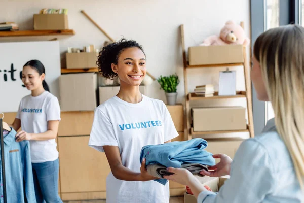 Foyer sélectif de sourire afro-américain volontaire donnant des vêtements à la femme — Photo de stock