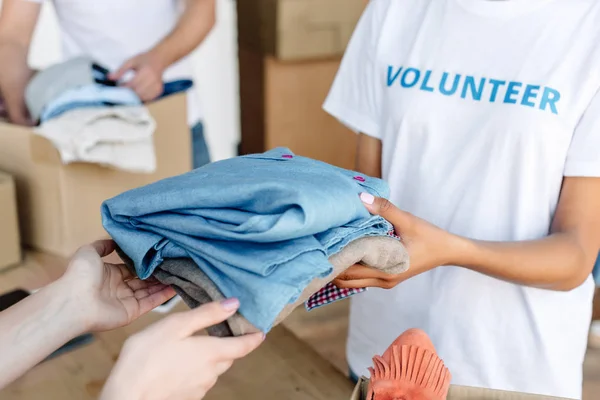 Visão cortada de voluntário dando roupas para a mulher no centro de caridade — Fotografia de Stock