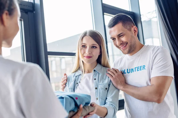 Selective focus of attractive blonde woman taking clothes from multicultural volunteers — Stock Photo