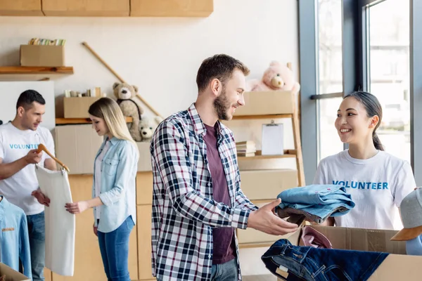 Selektiver Fokus junger multikultureller Freiwilliger, die Menschen in Wohltätigkeitszentren Kleidung geben — Stockfoto