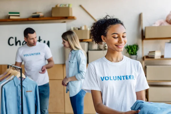 Selective focus of multicultural volunteers giving clothes to people in charity center — Stock Photo
