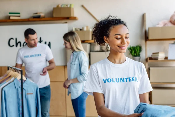 Enfoque selectivo de voluntarios multiculturales que dan ropa a las personas en el centro de caridad - foto de stock