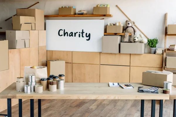 Wooden table with tins and paper cups, cardboard boxes and placard with charity inscription — Stock Photo