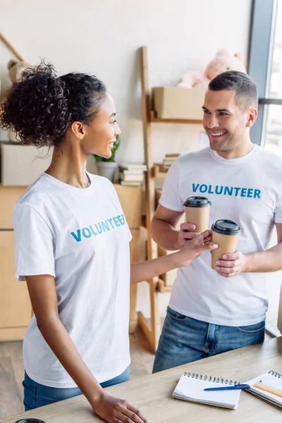 Alegres voluntarios multiculturales sonriendo y hablando mientras sostienen vasos de papel - foto de stock