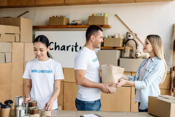 Jóvenes voluntarios multiculturales dando comida a mujeres bonitas en el centro de caridad - foto de stock