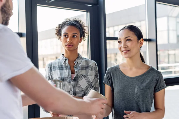 Pretty multicultural women taking canned food from volunteer in charity center — Stock Photo