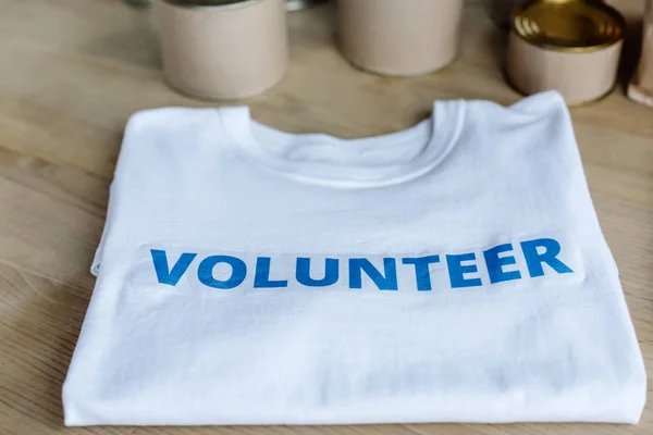 Selektiver Schwerpunkt weißes T-Shirt mit blauer Freiwilligenbeschriftung auf Holztisch — Stockfoto