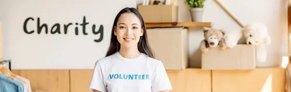 Tiro panoramico di bella, sorridente volontario asiatico vicino cartello con iscrizione di carità — Foto stock