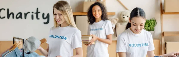 Panoramic shot of three beautiful multicultural volunteers working in charity center — Stock Photo
