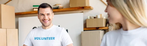 Panoramic shot of handsome, smiling volunteer looking at girl in charity center — Stock Photo