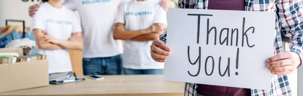 Plano panorámico del hombre que sostiene la tarjeta con la inscripción del agradecimiento mientras que está parado cerca de voluntarios - foto de stock