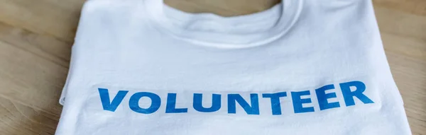 Panoramaaufnahme eines weißen T-Shirts mit blauer Freiwilligenbeschriftung auf einem Holztisch — Stockfoto