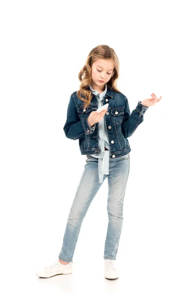 Vista completa de niño concentrado en ropa de mezclilla usando teléfono inteligente en blanco - foto de stock