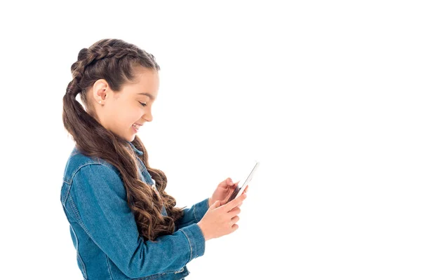 Vue latérale de l'enfant souriant en veste en denim à l'aide d'un smartphone isolé sur blanc — Photo de stock