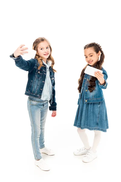 Vista completa de los niños en ropa de mezclilla tomando selfie en blanco - foto de stock